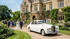 White vintage Rolls-curity wedding car decorated with ivory ribbon outside a UK country house venue